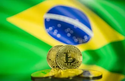 Moedas de Bitcoin douradas em primeiro plano, com a bandeira do Brasil desfocada ao fundo.