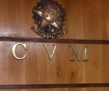 Foto do logo da CVM, em metal nobre, em uma parede de madeira