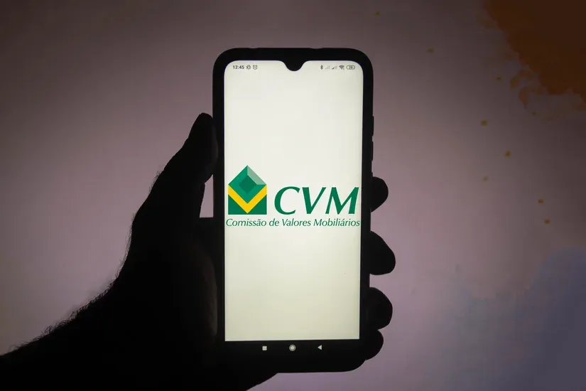 Celular em mãos exibindo o logotipo da CVM na tela